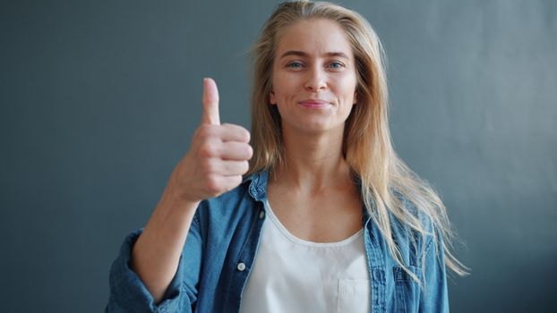 Portrait of a smiling woman giving a thumbs up against a neutral background.